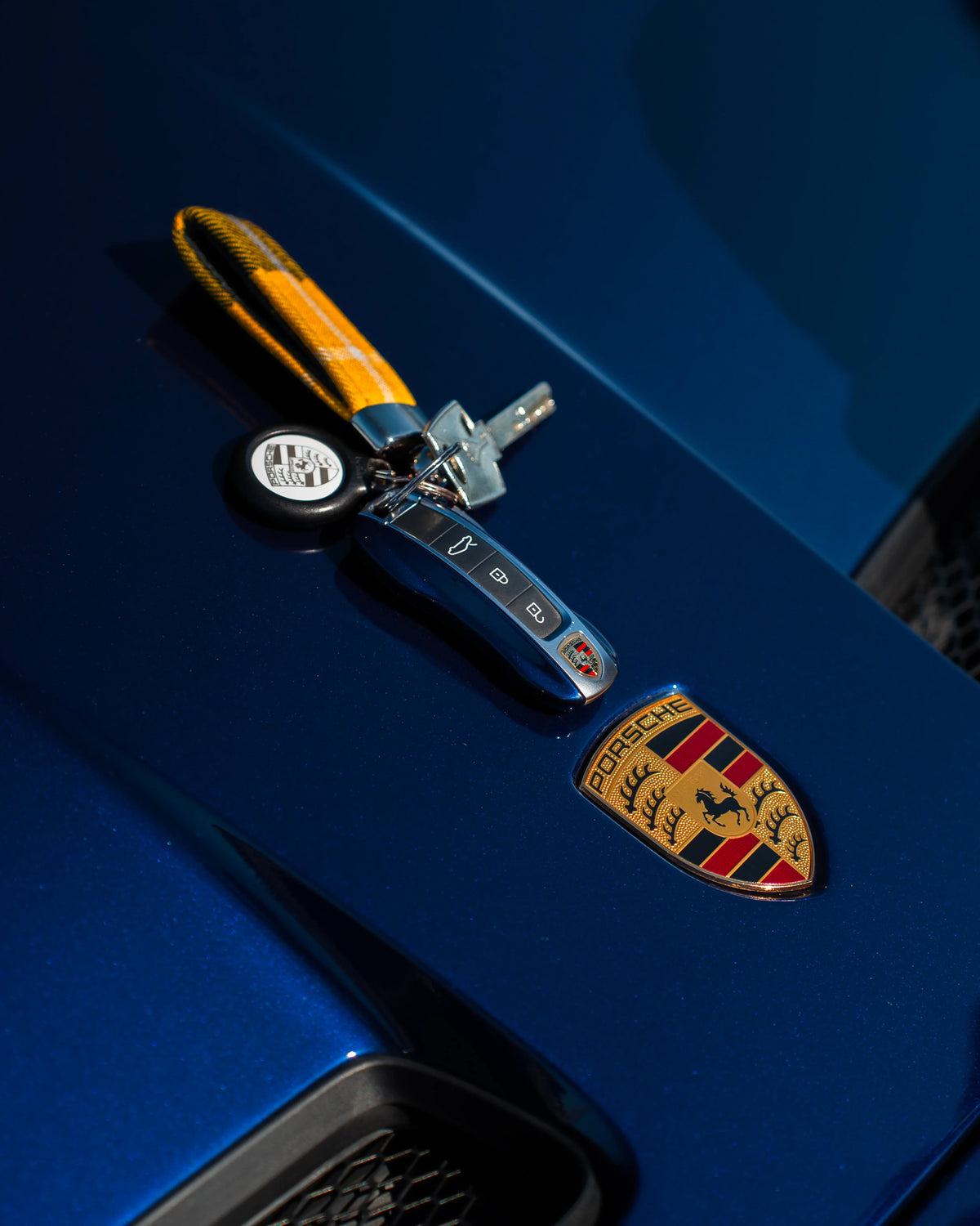 Clés de voiture Porsche posées sur capot bleu à logo Porsche, porte-clés jaune