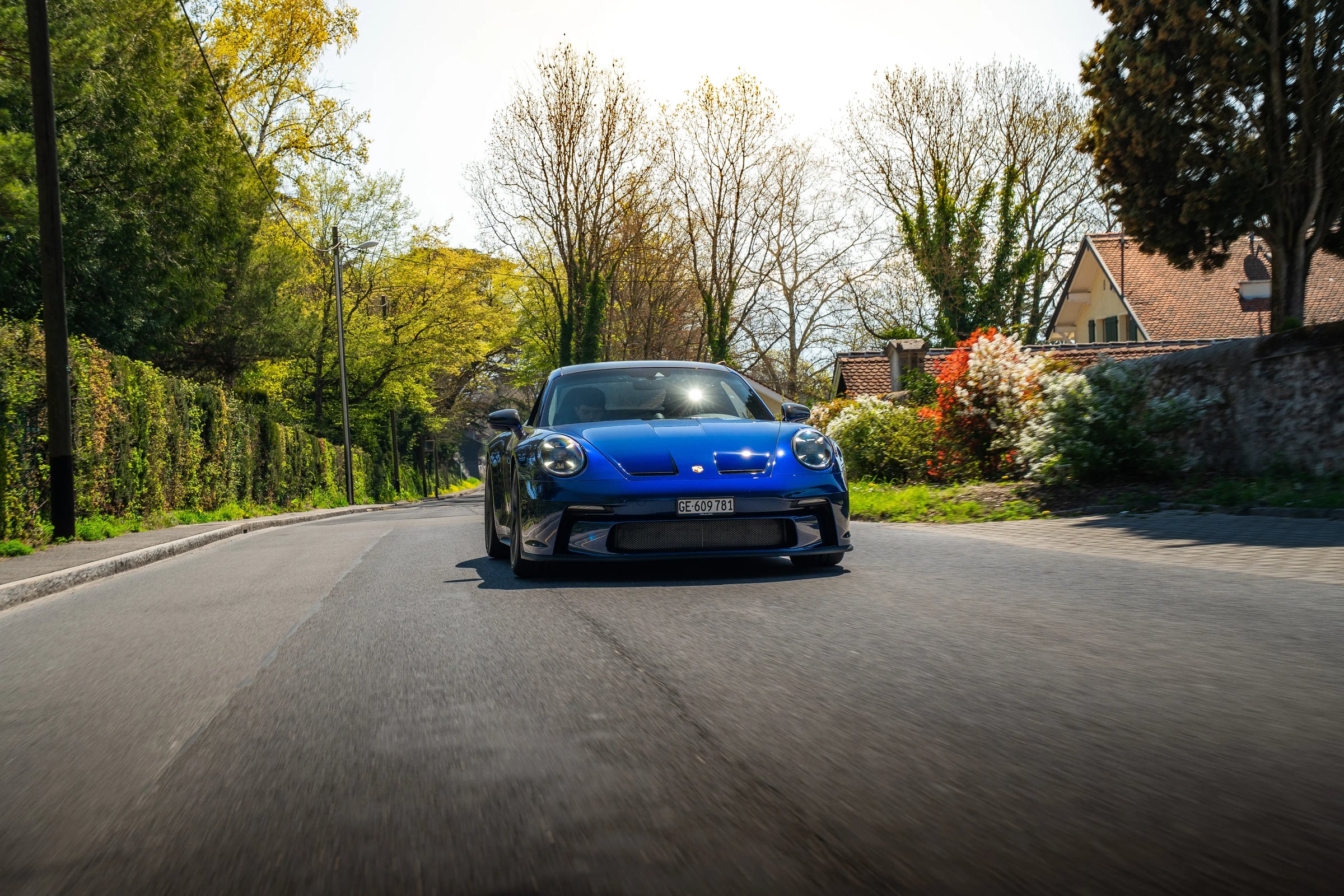 Porsche bleue sur route bordée d’arbres et de maisons en plein jour